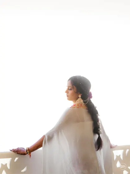 A serene, high-key portrait of the bride looking out from a balcony during her Haldi in Udaipur. The bright light creates an ethereal, dreamy mood.