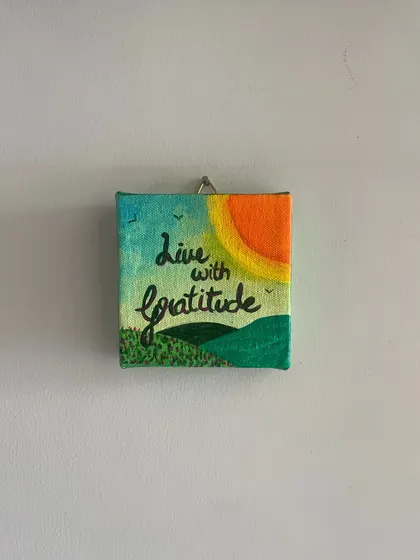 'Live with Gratitude'. This hand-painted mini canvas captures a simple, sunny landscape to serve as a daily reminder to appreciate the small joys in life. It's a little piece of sunshine for your wall.
