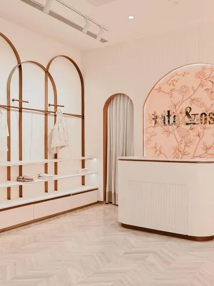 At Kate & Oscar, the customer journey begins at this welcoming reception desk. The curved form is set against a custom-illustrated backdrop, with arched clothing racks framing the space and hinting at the whimsical, gentle aesthetic of the store.
