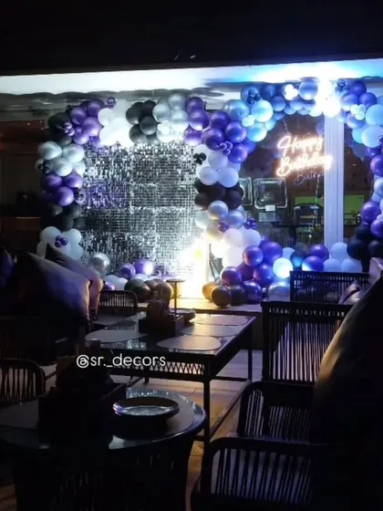 A moody and stylish party setup with a silver shimmer wall and a balloon ring in purple, black, and white.