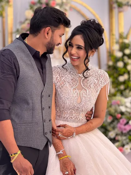 A happy couple at their reception. The bride is wearing a beautiful white gown with intricate beadwork, and her makeup is elegant and timeless.