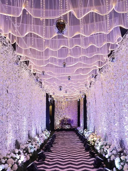 An ethereal sangeet entrance pathway with walls of baby's breath and a ceiling of soft, glowing fabric waves and disco balls.