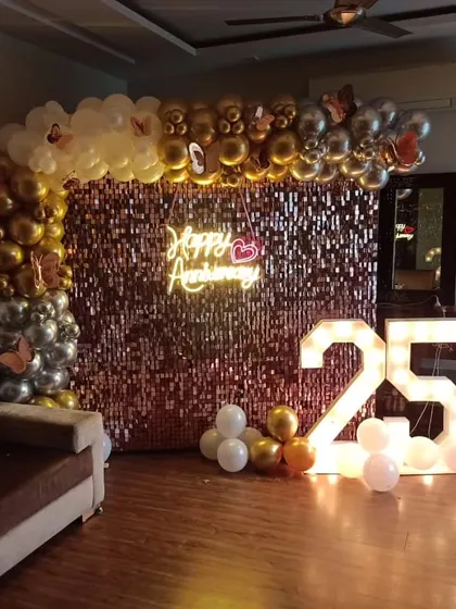 Celebrating a 25th anniversary in style. This rose gold sequin wall is decorated with a gold and silver balloon arch and a "Happy Anniversary" neon sign.