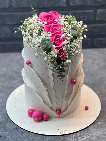 A modern white cake with a textured finish and a cascade of fresh baby's breath and vibrant pink roses. This design is both contemporary and romantic.