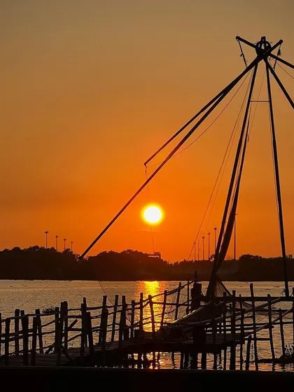 The iconic Chinese fishing nets of Kochi, Kerala, silhouetted against a warm sunset. This image captures a timeless tradition and the tranquil beauty of the backwaters, a story of culture meeting the coastline.