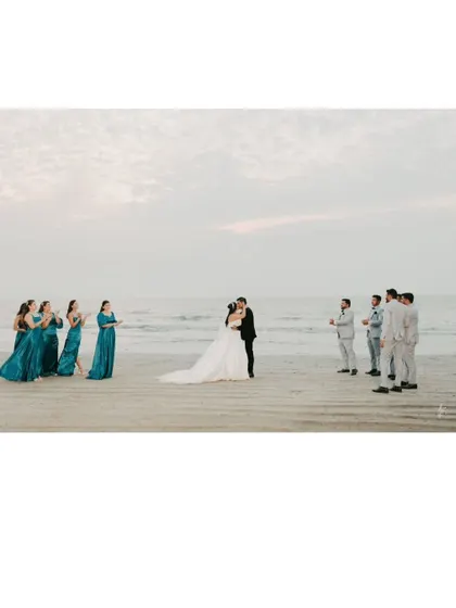 A wide shot of the couple kissing on the beach, framed by their applauding wedding party. A beautiful and celebratory destination wedding moment.