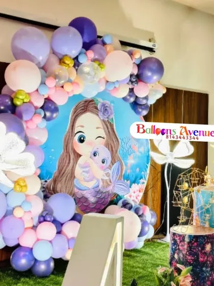 A mermaid-themed decoration featuring a large character backdrop and a purple and pink balloon arch, perfect for a vibrant celebration.