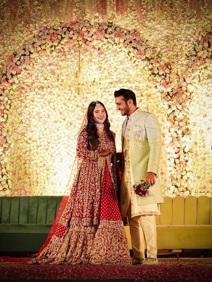 A beautiful couple portrait in front of a massive wall of flowers. The backdrop, filled with thousands of pink and white blossoms, creates a stunning and luxurious setting for wedding photos.