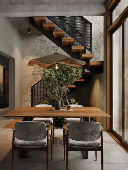 A dining area designed around an indoor tree, blurring the line between inside and out. The floating staircase and textured concrete wall add architectural character to the space.