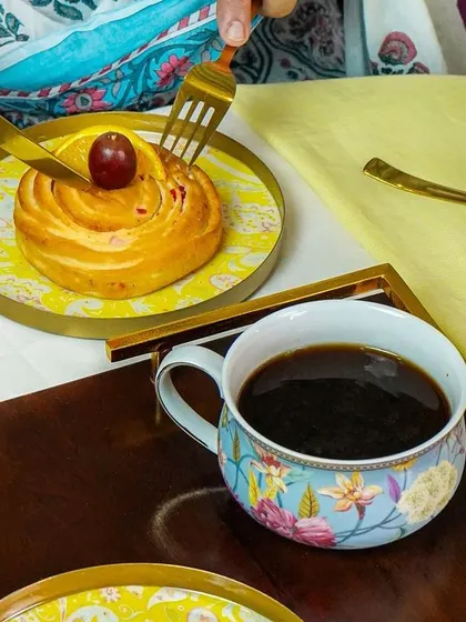 A close-up of someone cutting into a pastry, with a beautifully designed coffee cup and plate. This action shot is engaging and tells a story.