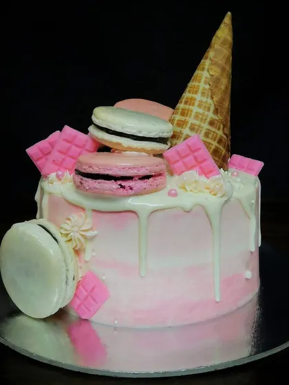 A fun and playful drip cake topped with an ice cream cone and delicious chocolate-filled macarons. The pink ombre and white drip make it a perfect treat for a sweet celebration.