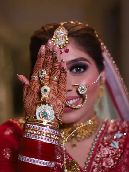 A creative bridal portrait where the bride playfully peeks from behind her hand, showcasing her eye makeup and detailed hand jewelry.