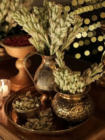 A close-up of traditional brass vases filled with tuberoses, set on a wooden table for a classic and elegant decor detail.