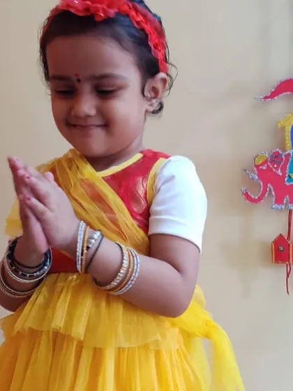 Dressed in festive yellow, this child's gentle 'Namaste' pose complements her beautiful handmade craft, blending art with grace and courtesy.