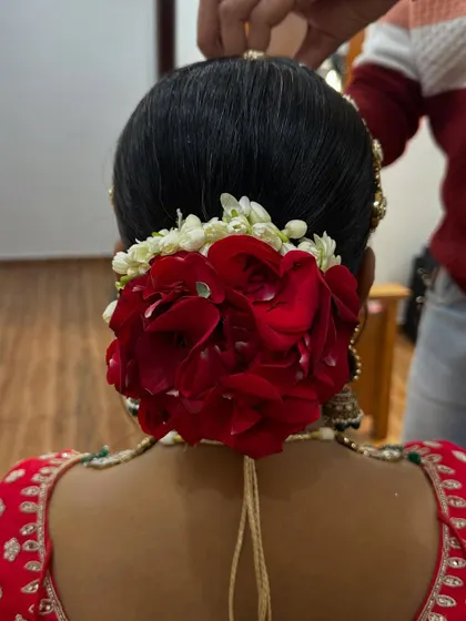A classic bridal hairstyle. This beautiful low bun is decorated with fresh red roses and jasmine, creating a timeless and elegant look for her wedding day.