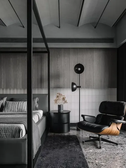 The master bedroom, featuring an Eames lounge chair that adds a classic design touch to the contemporary, monochrome space.