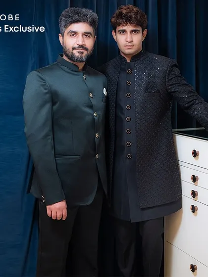 A duo showing off two distinct dark-toned outfits. One wears a quilted black Indo-western, while the other sports a sleek green Jodhpuri suit.