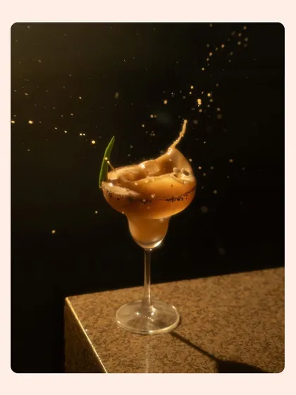 A dark and moody splash shot of a coffee-colored cocktail. The golden-hued droplets against the black background create a sense of luxury and excitement.