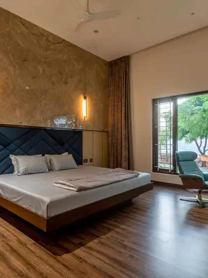 A luxurious bedroom with a custom-upholstered headboard, a marble accent wall, and a dedicated reading chair positioned by the window to enjoy the outdoor view.