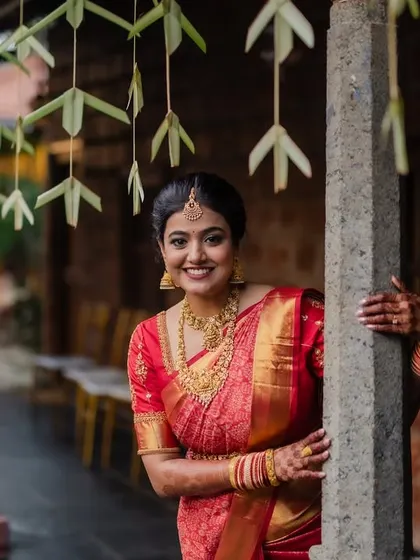 A portrait of the bride in her stunning red saree, framed by the rustic charm of her wedding venue. We focus on creating images that are both beautiful and full of character.