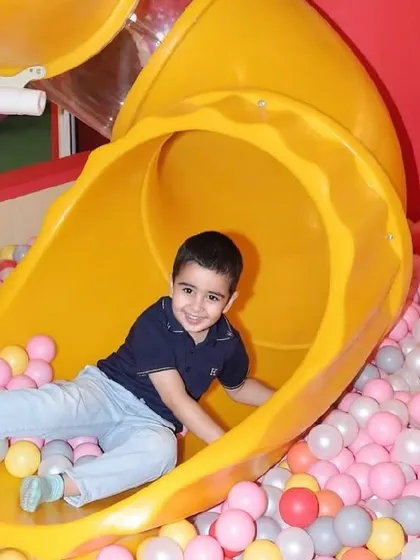 A happy boy smiles as he lands at the bottom of the tube slide and into the ball pit.