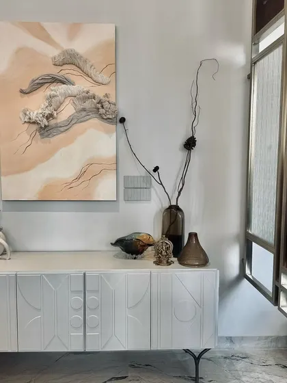 This vignette showcases our focus on curating details. A white console with geometric carvings is paired with a triptych of textured wall art, dried botanicals in minimalist vases, and small brass artifacts, creating a corner that is both serene and full of personality.