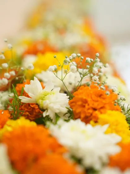 A close-up of the marigold and chrysanthemum garland. The vibrant orange and yellow of the marigolds are traditional symbols of celebration and auspiciousness in Indian culture.