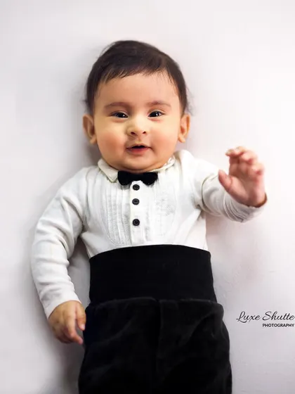 A five-month-old baby dressed in a tiny tuxedo shirt, looking curiously at the camera. This is a great example of a milestone session for a sitting baby.