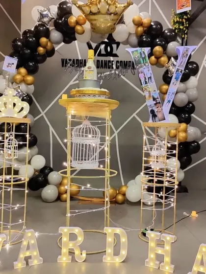 A sophisticated birthday setup for an adult celebration. This decor features a circular balloon arch in black, white, and gold, with lighted pedestals, marquee letters, and a custom initial filled with photos.