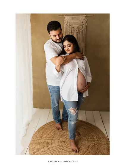 A minimalist and modern take on a maternity portrait. The couple, dressed in simple jeans and white shirts, shares an intimate moment in a bright, clean space.