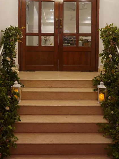 A simple yet elegant entrance for a home event. We wrapped the staircase railings in fresh greenery and placed lanterns with pillar candles at the base to create a warm and welcoming path for guests.