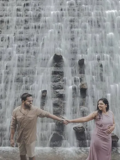 A couple holds hands before a stunning man-made waterfall, blending natural beauty with impressive scale for a unique pre-wedding shot.