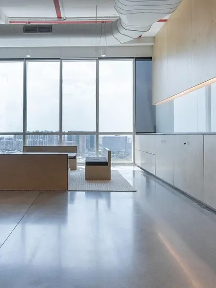 An uncluttered corner in a modern office, where polished concrete floors and birch plywood cabinetry create a clean, minimalist aesthetic. Large windows flood the space with natural light, embodying our principle of creating airy, open, and timeless interiors.
