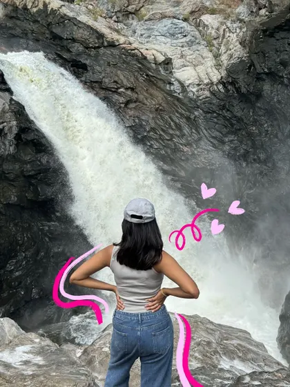 Standing before a waterfall, with a pink doodle adding a pop of color and energy to the powerful scene.