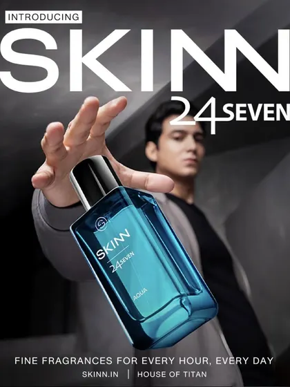 A commercial product shot for Skinn by Titan's fragrance line. The composition uses forced perspective to make the bottle the hero, while the model in the background provides a human element.