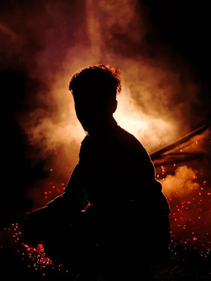 The silhouette of a person is framed by a cloud of red and orange smoke and embers. This dramatic, low-light image is full of energy and mystery.