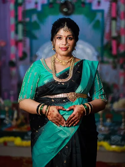 The beautiful mom-to-be showing her heart hands over her baby bump, with the rich stain of her baby shower mehendi clearly visible.