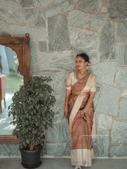A stunning full-length portrait of the bride against a stone wall. The natural textures of the background complement the rich fabric of her traditional saree.