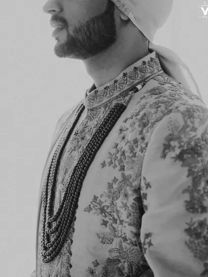 A detailed black and white shot of the groom's profile, highlighting the texture of his beard and the intricate embroidery on his sherwani. A classic and masculine portrait.