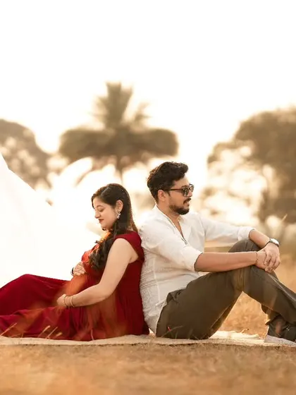 A creative outdoor shot of a couple sitting back-to-back, with a flowing white cloth adding a touch of artistry to the rustic, golden-hour scene.