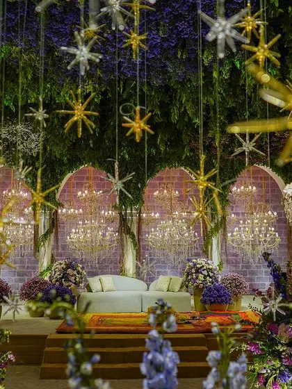 The main stage of our 'Lilac & Gold' themed event. The backdrop features brick-textured arches draped in ivy, with dozens of crystal chandeliers creating a sparkling curtain of light. The ceiling is a canopy of lush greenery and hanging stars.