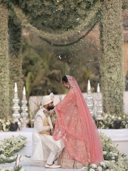 A tender moment during the varmala ceremony. The groom, on one knee, kisses his bride's hand under a shower of petals, a gesture of love and respect that I helped stage against a beautiful floral backdrop.