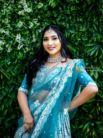 A close-up portrait against a green wall, making the sky blue color of the lehenga pop.