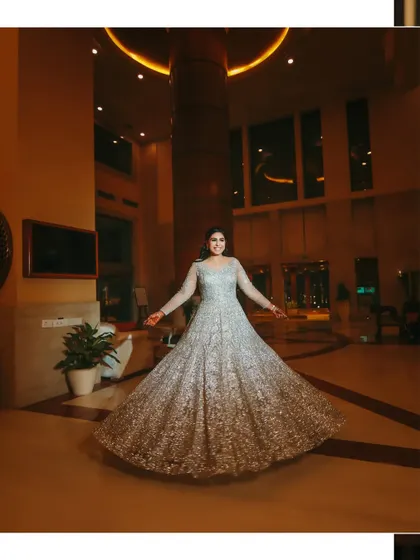 A joyful, twirling shot of the bride, showcasing the beautiful flare and shimmer of her silver reception gown in a grand hotel lobby.