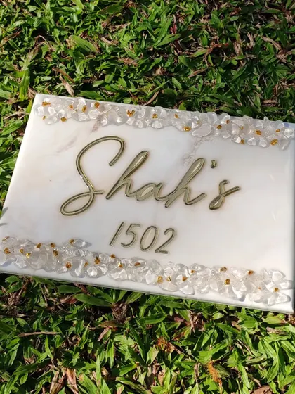 Displaying a custom marble effect nameplate outdoors to show how the natural light interacts with the glossy resin and embedded stones. The piece is durable enough for outdoor display at a home's entrance.