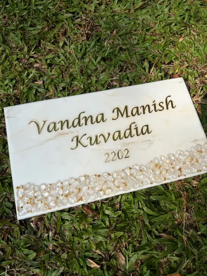 This rectangular nameplate features a white marble effect with a border of natural stones on the bottom edge. The clean design is perfect for a modern home, providing an elegant and personalized touch.