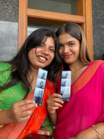 Two friends in vibrant sarees, smiling with their photo strips.
