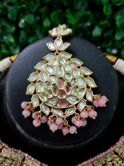 A close-up of a maang tikka with pink kundan work and matching pink bead drops, part of a modern bridal set.
