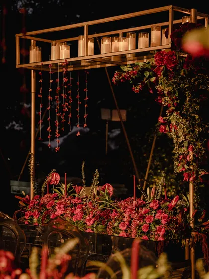 The bar and food station was designed as a statement piece, with a modern gold structure, hanging floral tassels, and a dense arrangement of red flowers. It was both a functional station and a beautiful decor element.
