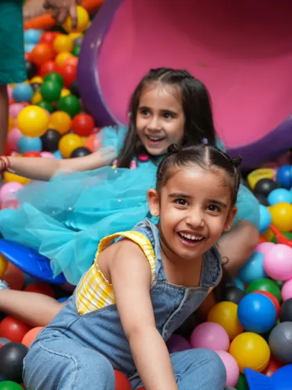 Say cheese! Two friends smile brightly while having fun together in the colorful ball pit.